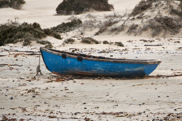 Simple wooden fishing boat tied up with a chain on the beach.
