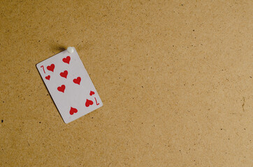The playing card of the seven hearts is attached to a brown surface. The card is punctuated with a...