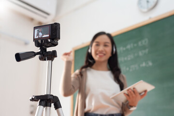 Selective focus, Smiling Asian Young woman teacher teaching and recording video with digital camera