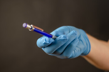 Defocused shot of doctor's hand in blue medical glove with pencil. Hand is holding mechanical pencil against black background. Selective focus. Close-up. Blurred, defocus, noise, grain effect