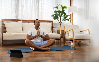 African American man practicing yoga and meditating in lotus position at home.