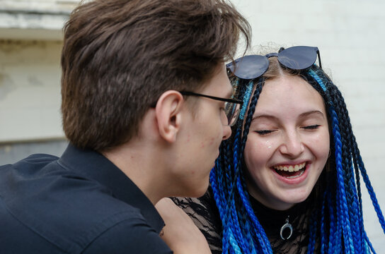 Naughty cheerful young woman with a toothy smile. The female with long blue pigtails laughs happily. A young male stands beside her. Love, relationships. Selective focus.