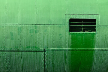 The side of an old military submarine with welded seams, rivets and a grille