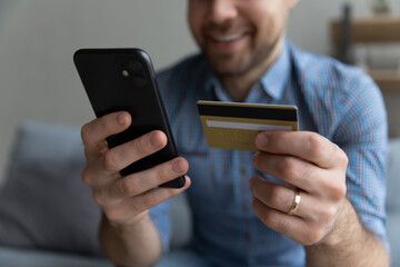 Crop close up smiling man paying online by gold credit card, satisfied client browsing internet banking service, young male customer making secure internet payment, shopping online at home