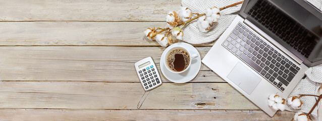 laptop computer, coffee and calculator on a rustic wooden office desk with cotton branches, business and finance accounting in autumn, panoramic format, copy space, flat lay from above