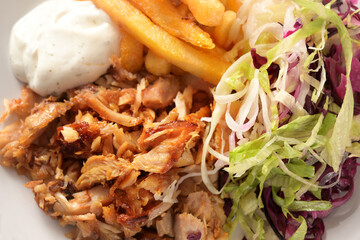 Roasted doner kebab chicken meat with french fries, salad and tzatziki dip, high angle view from above, full frame close-up shot, selected focus