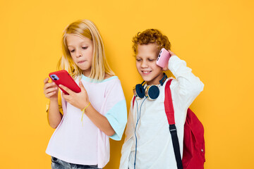 Two kids boy and girl use gadgets with headphones yellow background