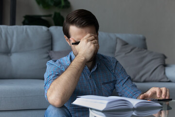 Unhappy man calculating domestic bills at home, upset by financial problem, unexpected debt or bankruptcy, frustrated young male covering face with hand, lack of money and high taxes concept
