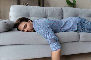 Exhausted man lying on comfortable couch at home, sleeping, taking day nap or daydreaming, tired...