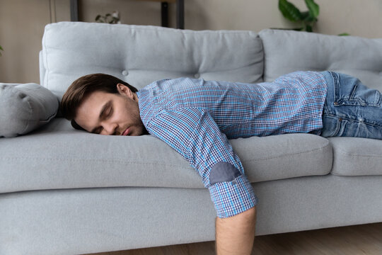 Exhausted Man Lying On Comfortable Couch At Home, Sleeping, Taking Day Nap Or Daydreaming, Tired Overworked Young Male Fall Asleep On Sofa After Difficult Working Day, Fatigue And Tiredness Concept