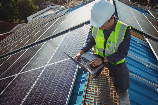 Electric engineer working white safety on height building, installing solar panels on the rooftop working using notebook computer, inspecting, measuring, collecting data for repairing