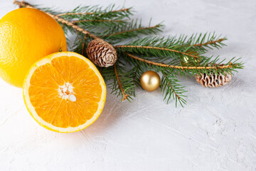 Fototapeta na wymiar Oranges with a spruce branch with Christmas balls and cones on a light background. Christmas and New Year concept.