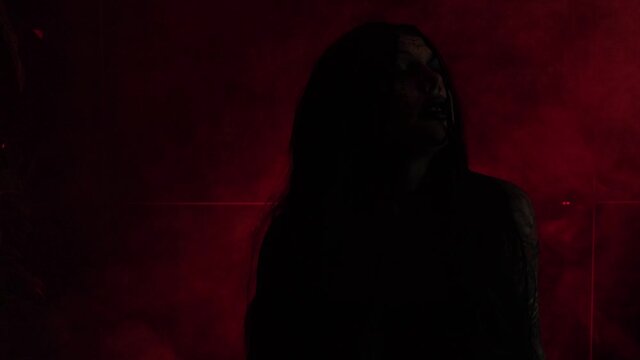 Silhouette of a witch with shimmering light with smoke and red light.