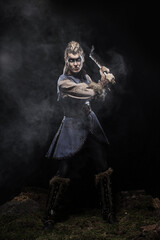Woman viking warrior in history costume with ax aggressively attacks on dark background