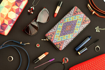 Accessories for creating a feminine style. Accessories for a fashionable look. Wallets, sunglasses, lipstick, mascara, bijouterie on a black background.