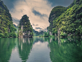 Fototapeta na wymiar Spectacular landscape in Ninh Binh with mountains, caves and boat tour on river. Exotic tropical landscape with hills and river. 