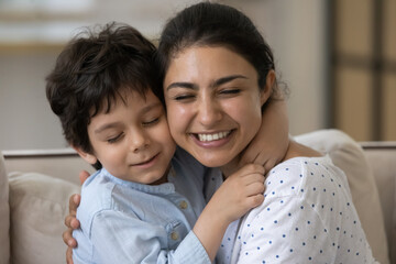 Affectionate happy young indian mother cuddling cute small kid son, showing sweet tender loving feelings, missing after long separation, joyful asian family enjoying peaceful time together at home.