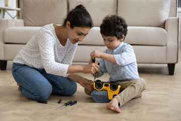 Happy young indian mother helping adorable small kid son fixing toy car with screwdriver, playing...