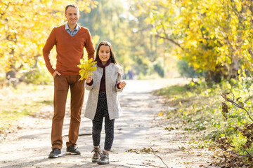 Obraz premium Adorable little girl with happy father walking in autumn park on a sunny day