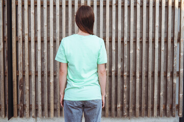 Young female with long hair wears green t-shirt and posing against a background, back view.