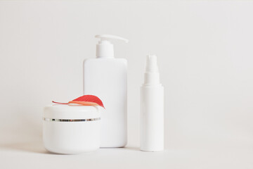 blank white bottles for cosmetics, mock up cream jar and red autumn fallen leaves on a beige light background