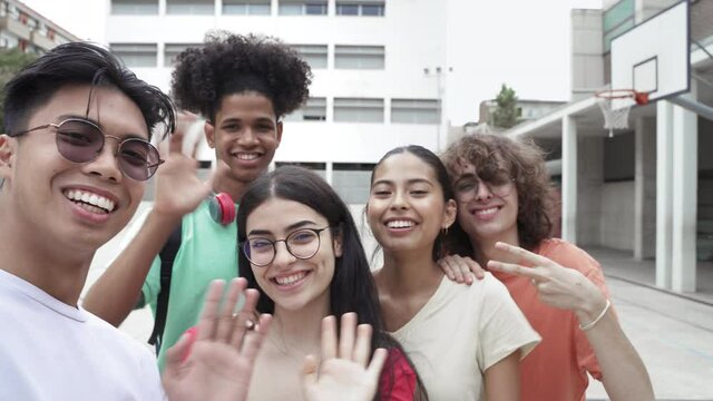 Asian young guy and group of multi ethnic teenager friends taking selfie photo with phone looking to camera. Happy students saying hello greetings in Secondary School 