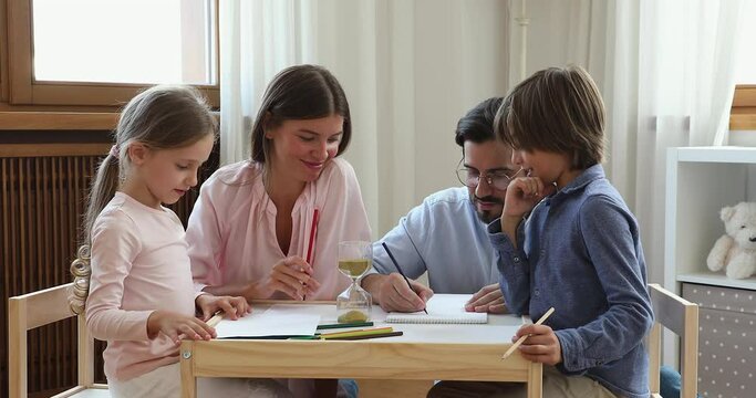 Family time. Happy young couple play brain developing hobby game with preteen daughter son at home weekend. Loving mom dad spend free time together with children boy girl have fun enjoy table top game