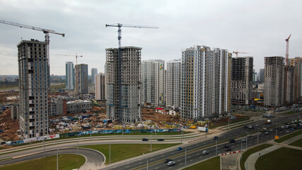 Naklejka premium Construction of modern multi-storey buildings. Construction of a new city block. Buildings under construction and tower cranes. Aerial photography in cloudy weather.