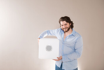 Young attractive man  holding white portable bluetooth speaker on gray background