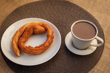 Plate with churros next to a cup of chocolate on a checkered tablecloth.