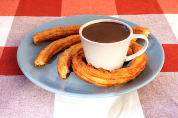 Plate with a cup of chocolate and churros surrounding the cup, breakfast or snack in Andalusia, Spain.