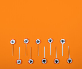 Halloween candy row with black spiders and cobweb on orange color background,top view