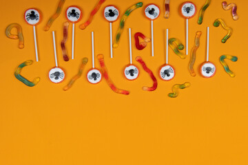 Halloween candy with black spiders,cobweb and tasty jelly worms on orange color background,top view