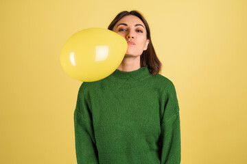 Young woman in green warm sweater happy funny playful blowing air balloon