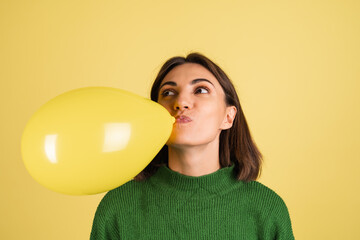 Young woman in green warm sweater happy funny playful blowing air balloon