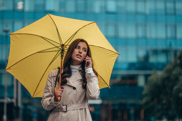 Woman using smartphone and holding a yellow umbrella during a heavy rain in the city