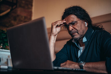Senior hispanic cuban men having a headache while using a laptop