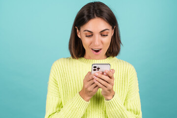 Young woman in light green sweater with mobile phone look at screen shocked excited surprised