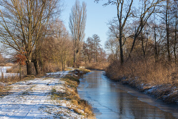 Fototapeta na wymiar Winter landscape. Road on which there is white snow. A stream flows along the road.