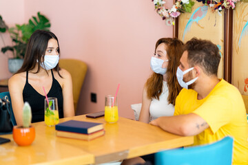 Obraz na płótnie Canvas Grop of friends chatting and smiling while they sitting and drinking some beverage in a cafe with medical face mask. Corona virus outbreaking.
