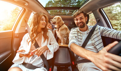 The whole family is driving for the weekend. Mom and Dad with their daughter and a Labrador dog are...