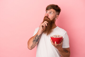 Young caucasian ginger man with long beard holding a bowl of cereales isolated on pink background...