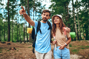 Obraz premium A loving couple of hikers with backpacks walk through a pine forest. Camping, travel, hiking.