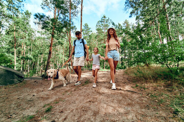Happy family with backpacks and labrador dog are walking in the forest. Camping, travel, hiking.
