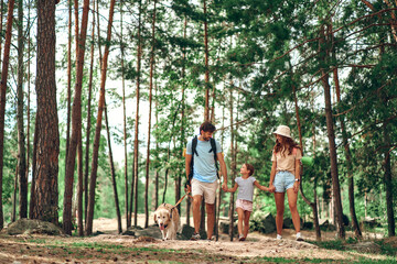 Happy family with backpacks and labrador dog walks in the forest. Camping, travel, hiking.