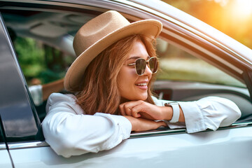 A woman in a hat and sunglasses looks out of the car window and relaxes. Buying a car. Travel,...