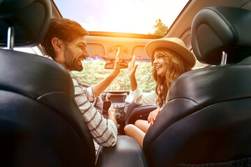 A young couple are giving five to each other in a new car. A man driving a car with his girlfriend and having fun. Buying and renting a car. Travel, tourism, recreation. - Powered by Adobe