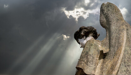 Figure of a stone angel, under a dark sky through which rays of light are coming out.