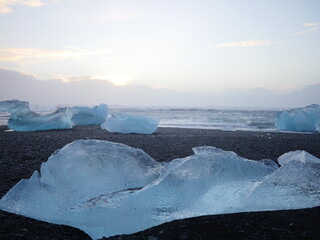 Pure blue ice bergs in Iceland washed ashore by sea waves. Background is a sunset pastel colored sky with cloud.