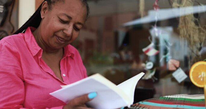 Mature african woman reading a book at bar outdoor 